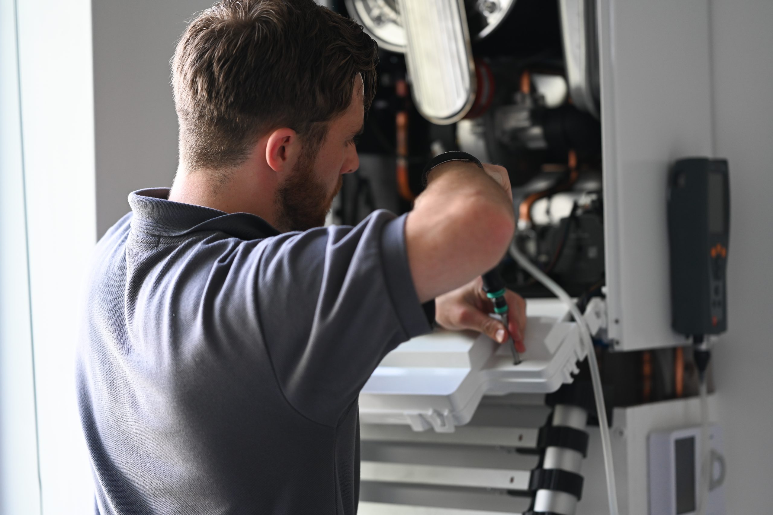 Refresh NI Gas Safe Engineer working on a white boiler unit wearing a grey Refresh NI branded Polo top.